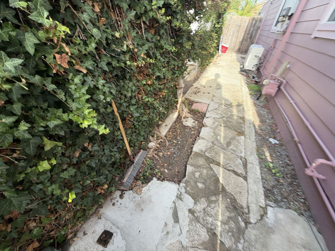 Cracked, broken side yard walkway with uneven slabs and loose pavers